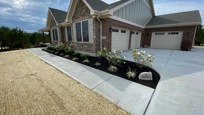 New landscape bed along sidewalk beside brick home with garages